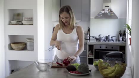 Cheerful-young-pregnant-woman-cooking-at-kitchen